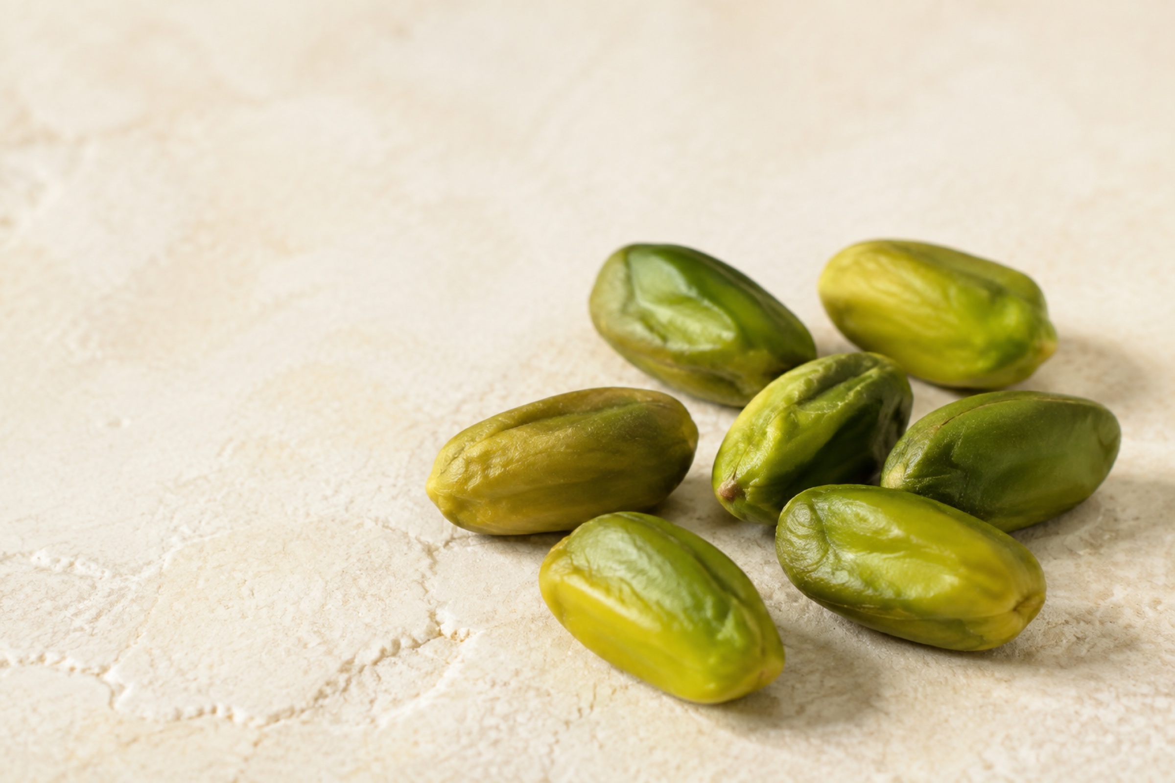 Seven peeled green pistachio kernels on a warm ivory surface